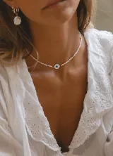 Gargantilla de cristalitos facetados blancos y dorados, con dije central de ojo turco esmaltado en acero.