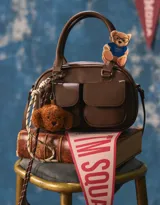 Cartera bowling marrón chocolate de cuerina con doble bolsillo frontal con solapa y broche, cierre superior, correa regulable y desmontable, manijas superiores y charm de perrito.
