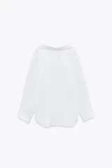 Camisa negra de cuello solapa y manga larga amplia. Tiene un bolsillo de parche en el delantero, detalle de pliegues y cierre frontal con botones.