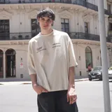 Remera beige claro de algodón, corte oversize, con estampado en la espalda que incluye la inscripción "Venefo Industries Company" y otros textos.