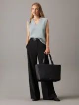 Bolso tote negro Calvin Klein, confeccionado en piel sintética acolchada con diseño de rayas verticales. Tiene doble asa de hombro, cierre superior con cremallera, herrajes plateados y logo metálico en el frente.