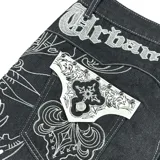 Bermuda de denim negro con bordados blancos estilo barroco/rococó en los bolsillos traseros y a lo largo de los costados. Presenta costuras contrastantes blancas, tiro medio y calce holgado (baggy fit). En la parte superior trasera lleva un aplique con el texto "Urban Coutur".