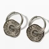 Aros tipo argolla de acero plateado con dije circular calado con diseño de rayos.