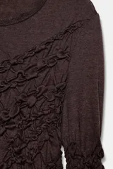 Vestido midi color marrón oscuro, con cuello redondo y manga larga. Presenta frunces diagonales en la parte superior delantera y en las mangas, y un bajo asimétrico.