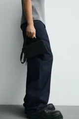 Bandolera negra con acabado engomado, compartimento principal con cierre de cremallera y bolsillo interior con cremallera. Asa de hombro ajustable y extraíble.