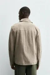 Cazadora de hombre de corte regular fit, confeccionada en piel con acabado ante color beige claro. Presenta cuello solapa, manga larga con puño de botón, bolsillos de plastrón en la cadera y cierre frontal con botonadura.