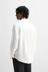 Camisa color arena de lino con cuello abotonado, manga larga con puños abotonados, corte regular y bajo con aberturas laterales.