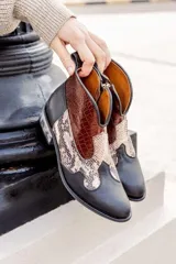 Botines de cuero negro con detalles en cuero marrón con textura de cocodrilo en la caña y cuero con estampado de piel de serpiente en el empeine. Cierre lateral con cremallera y tacón bajo. Estilo cowboy.