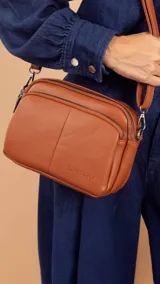 Bandolera color gris oscuro con doble bolsillo principal, un bolsillo frontal y uno trasero, todos con cierre. Incluye correa ajustable y logo de la marca "Lincoln's" grabado en el frente.