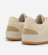 Championes casuales de caña baja, color beige y crema, con suela tipo caja. Presentan una combinación de materiales lisos y gamuza sintética, perforaciones en la punta para ventilación, cierre de cordones y punta redondeada.