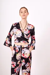 Camisa estampada con flores de colores sobre fondo negro, de corte cruzado, mangas 3/4 acampanadas y escote en V.