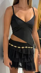 Top negro de tirantes finos, con escote pronunciado en V y diseño asimétrico en el bajo, estilo peplum corto.