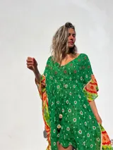 Túnica corta verde con estampado de flores blancas y detalles bordados en el escote. Mangas anchas con terminación en tela estampada a rayas naranjas y blancas.