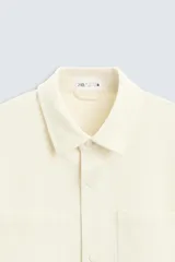 Sobrecamisa negra de tejido con elasticidad, cuello solapa, manga larga con puño abotonado, bolsillos de plastrón en el pecho y cierre frontal con botones a presión.