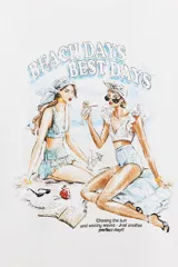 Camiseta blanca de corte recto y manga corta, con cuello redondo. Estampado frontal con dos mujeres en la playa y texto "Beach Days Best Days".