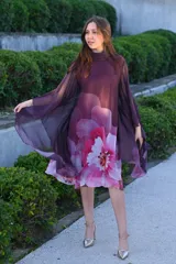 Vestido corto con cuello alto y mangas anchas, color morado con estampado floral en tonos rosados y blancos.