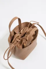 Bolso tote pequeño color visón de piel granulada con doble asa corta y correa bandolera ajustable y extraíble. Incluye bolsa interior ajustable con cordones. Logotipo de la marca grabado en el frente.