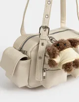 Cartera bandolera color crema con múltiples bolsillos frontales y laterales, doble asa corta regulable y charm de oso de peluche.
