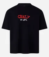 Remera negra de algodón con corte boxy, cuello redondo y mangas cortas. Estampado en la espalda de Lola Bunny besando a Bugs Bunny, con corazones y texto "Lola and Bugs Bunny".