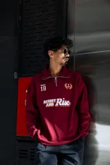 Buzo de algodón color bordó, estilo universitario, con cierre medio frontal y cuello alto. Estampado frontal con el texto "Since 19" y un ancla con laureles en amarillo y blanco.