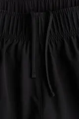 Short de correr negro de doble capa, con cintura elástica y cordón ajustable. Cuenta con una abertura lateral y un short interior con bolsillo en una pierna.