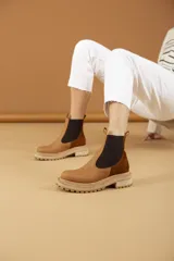 Bota Chelsea color marrón con paneles laterales elásticos negros, suela track color beige y tiradores en la parte superior.