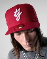 Gorra estilo 59FIFTY de visera plana, color rojo, con bordado frontal en hilo blanco que simula una firma o monograma estilizado.