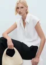 Camisa blanca sin mangas con cuello camisero y cierre frontal con botones.