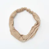 Diadema color beige de gasa de algodón con detalle de nudo en la parte delantera y elástico en la parte trasera.