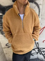 Buzo color beige de tela símil corderito, con cuello alto, cierre a mitad del torso y bolsillo tipo canguro.