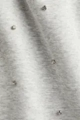 Minifalda gris melange de tejido suave con efecto neopreno y strass brillante. Tiene corte holgado, cintura elastizada con cordón ajustable y no está forrada.