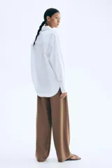 Pantalón sastrero marrón de punto con tiro alto, elástico oculto en la cintura, cierre decorativo, cinturón cosido con anillas en D de metal en un lateral y piernas ajustadas con pinzas para estilizar la silueta.