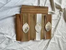 Billetera tipo sobre de ecocuero color beige con textura craquelada y solapa con aplique de cuero liso y botón de guampa.