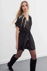 Minivestido negro de escote cruzado, mangas cortas y cintura elastizada con lazo. Presenta cadenitas metálicas en los hombros y en los extremos del lazo.