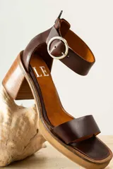 Sandalias de cuero color crudo, con tira ancha sobre los dedos, pulsera con hebilla al tobillo y taco cuadrado de madera.