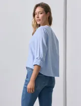 Blusa de algodón a rayas verticales finas en tonos blanco y lila, con escote en V, abertura frontal con botones y mangas largas regulables con presilla y botón. El ruedo termina anudado al frente.