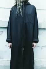 Parka larga negra con capucha ajustable con cordones, mangas largas con puños elásticos, bolsillos laterales y de plastrón en el pecho, bajo ajustable con cordón elástico y cierre frontal con cremallera metálica.