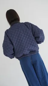 Campera puffer azul marino con diseño acolchado de rombos, cuello de cuero sintético negro, mangas largas abullonadas con puños elásticos y cierre frontal con cremallera.