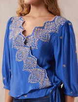 Blusa azul con bordados color crema, escote en V cruzado, mangas 3/4 abullonadas y nudo en el ruedo.