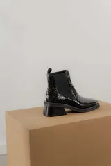 Bota negra de diseño clásico con detalles sofisticados, punta cuadrada y puntera metálica, con elásticos laterales para facilitar el calzado.