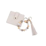 Llavero con pulsera de cuentas en tonos neutros, flecos de cuero sintético y tarjetero blanco con broche dorado.