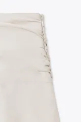 Falda pantalón color crema, de tiro medio, con volantes en capas y cierre lateral con cremallera.