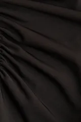 Remera negra de punto crepé con escote redondo y mangas cortas. Diseño ajustado con frunces en un hombro y en el lado opuesto de la cintura para crear un leve efecto drapeado.