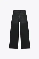 Pantalón de jean celeste de tiro alto, corte wide leg y largo hasta el tobillo. Presenta un diseño asimétrico en la cintura con cierre frontal cruzado con cremallera y botones metálicos.