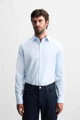 Camisa celeste de corte regular, con cuello italiano, mangas largas con puños abotonados y cierre frontal con botones.