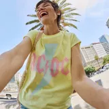 Camiseta amarilla de manga corta con estampado del logo de la banda AC/DC en rosa y celeste.