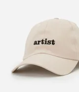 Gorra de sarga color beige con visera curva y bordado frontal con la palabra "artist" en negro.