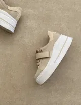 Zapatillas deportivas urbanas con capellada negra, detalles en beige y suela blanca.