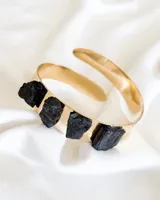 Brazalete rígido dorado con cuatro piedras de turmalina negra incrustadas.