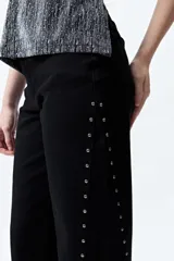 Pantalón de denim blanco con calce wide leg y ruedo desflecado. Presenta tachas metálicas a lo largo de los laterales.